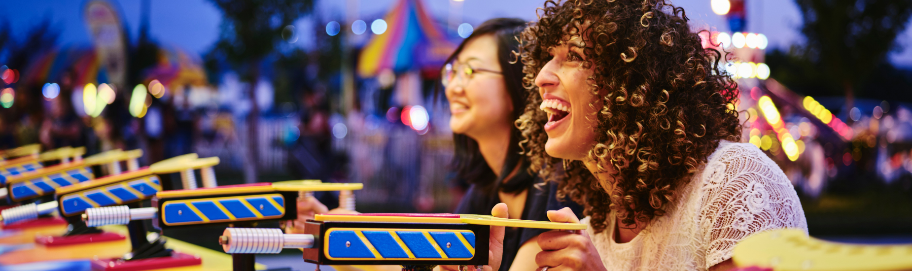 Friends enjoying a carefree moment at a summer carnival, laughing while playing a water game under bright lights.